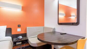 Habitación de hotel con una mesa redonda, dos sillas, un escritorio pequeño con un teléfono y un espejo en la pared.