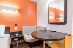 A hotel room with a round table, two chairs, a small desk with a telephone, and a mirror on the wall.