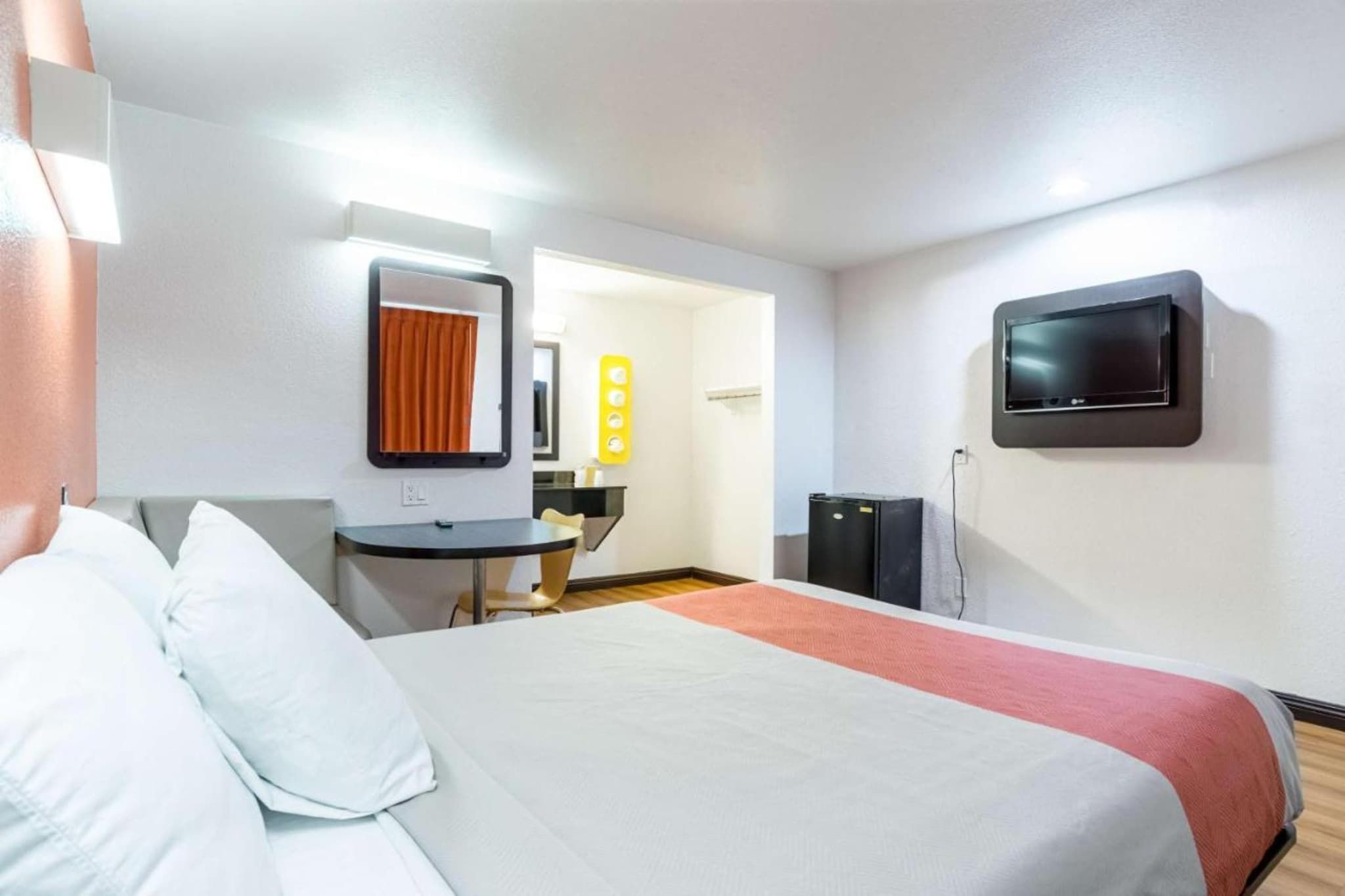 A hotel room with a bed, a desk, a chair, a television, and a mirror.