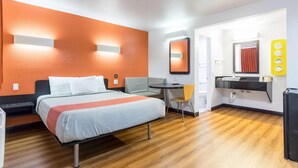A hotel room with a bed, a desk, a chair, a mirror, and a bathroom with a sink and toilet. - 1 QUEEN BED | Nsmk, MINI FRIDGE (Riverside)