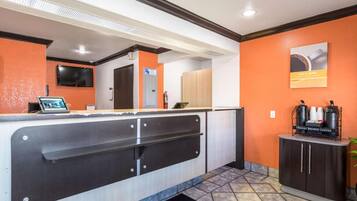 A reception area with a counter, a fire extinguisher, a coffee station, and a door with a sign.