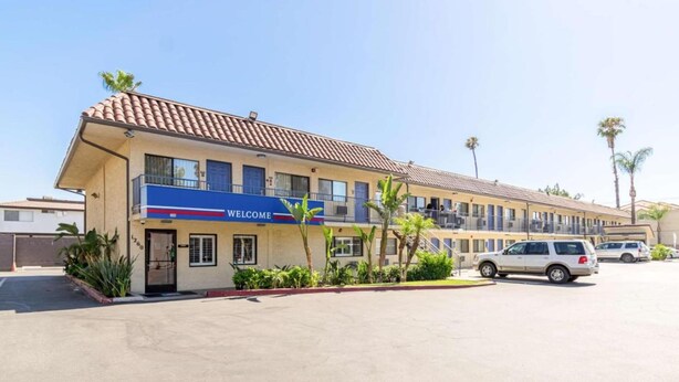 A hotel with a 'WELCOME' sign, multiple floors, and a parking lot with cars. - 1 QUEEN BED | Nsmk, MINI FRIDGE (Riverside)