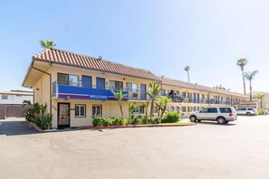 A hotel with a 'WELCOME' sign, multiple floors, and a parking lot with cars.