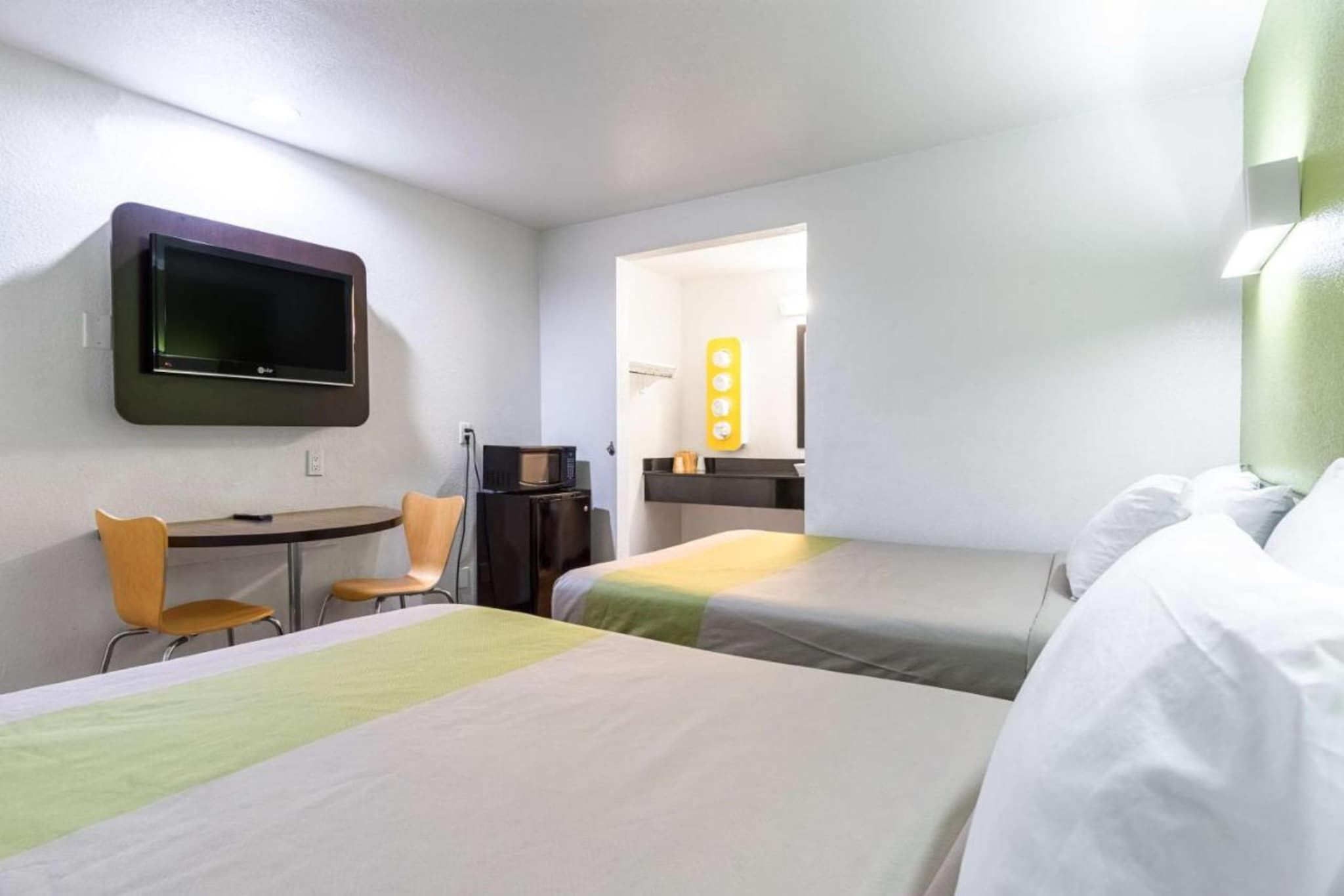 A hotel room with two beds, a desk, a chair, a television, and a bathroom visible through an open door.