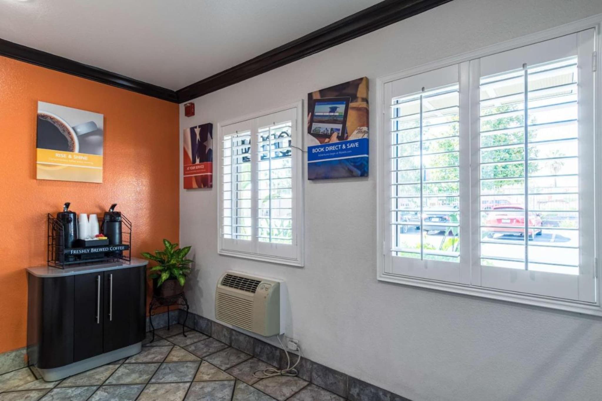 A reception area with a coffee station, a potted plant, and informational posters on the wall.