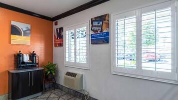 A reception area with a coffee station, a potted plant, and informational posters on the wall.