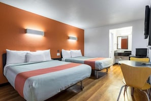 Ein Hotelzimmer mit zwei Betten, einem Schreibtisch, einem Stuhl und einem Fernseher.