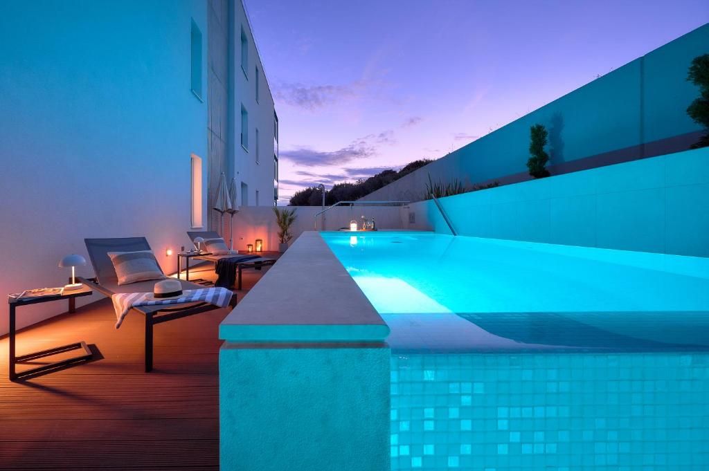 A pool area with lounge chairs and a table, surrounded by a low wall and a building.