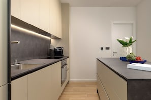 Uma cozinha moderna com bancada preta, eletrodomésticos de aço inoxidável e um vaso com flores na ilha.