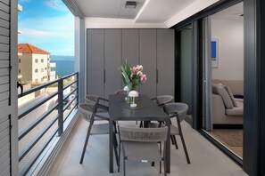Ein Balkon mit Tisch und Stühlen, einer Blumenvase und Blick auf Gebäude und das Meer.