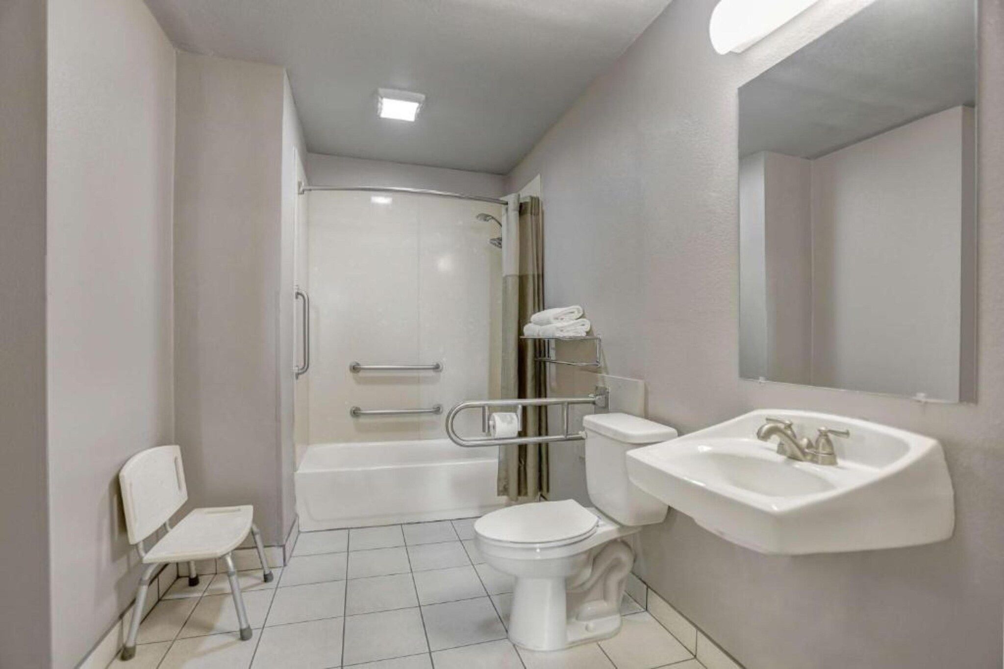 A bathroom with a shower, toilet, sink, and a chair.