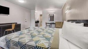 Habitación de hotel con cama, escritorio, silla, televisor y baño visible a través de una puerta abierta.