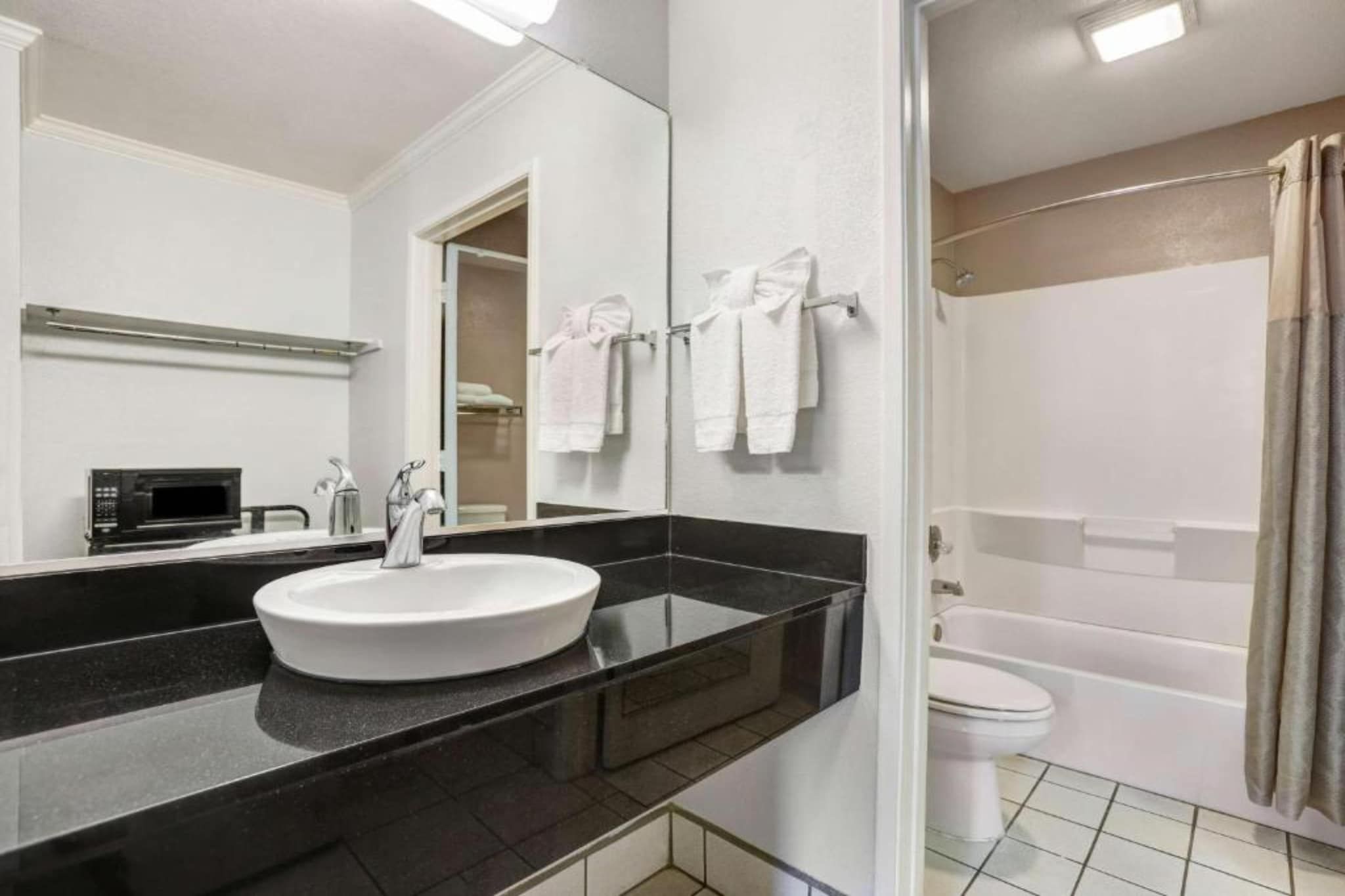 A modern bathroom with a black countertop, white sink, and a shower area.