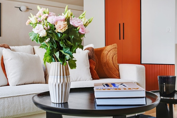 Una sala de estar con un sofá, una mesa redonda de centro, un jarrón con flores y un libro.
