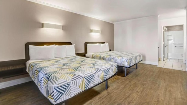 Habitación de hotel con dos camas, cada una con una colcha estampada, un cabecero de madera y una lámpara de pared.