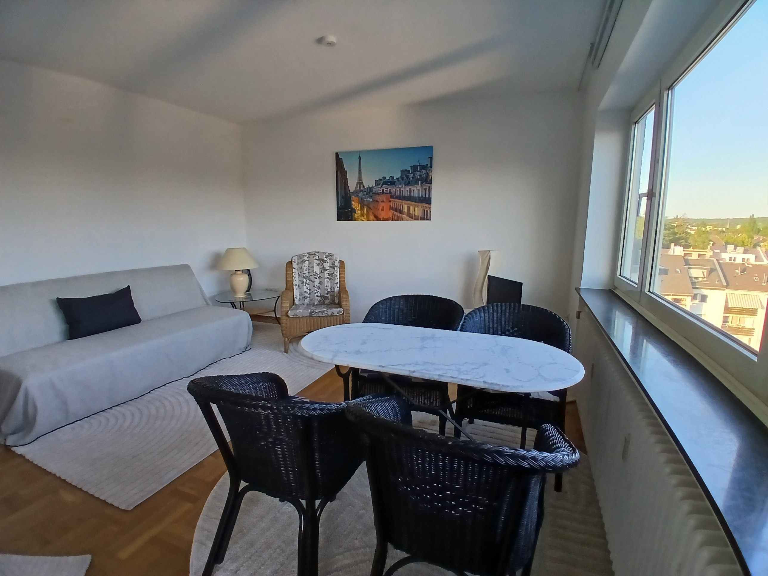 A modern living room with a sofa, a round table, and chairs, a lamp, and a painting on the wall.