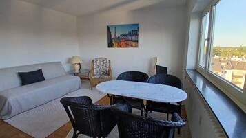 A modern living room with a sofa, a round table, and chairs, a lamp, and a painting on the wall.