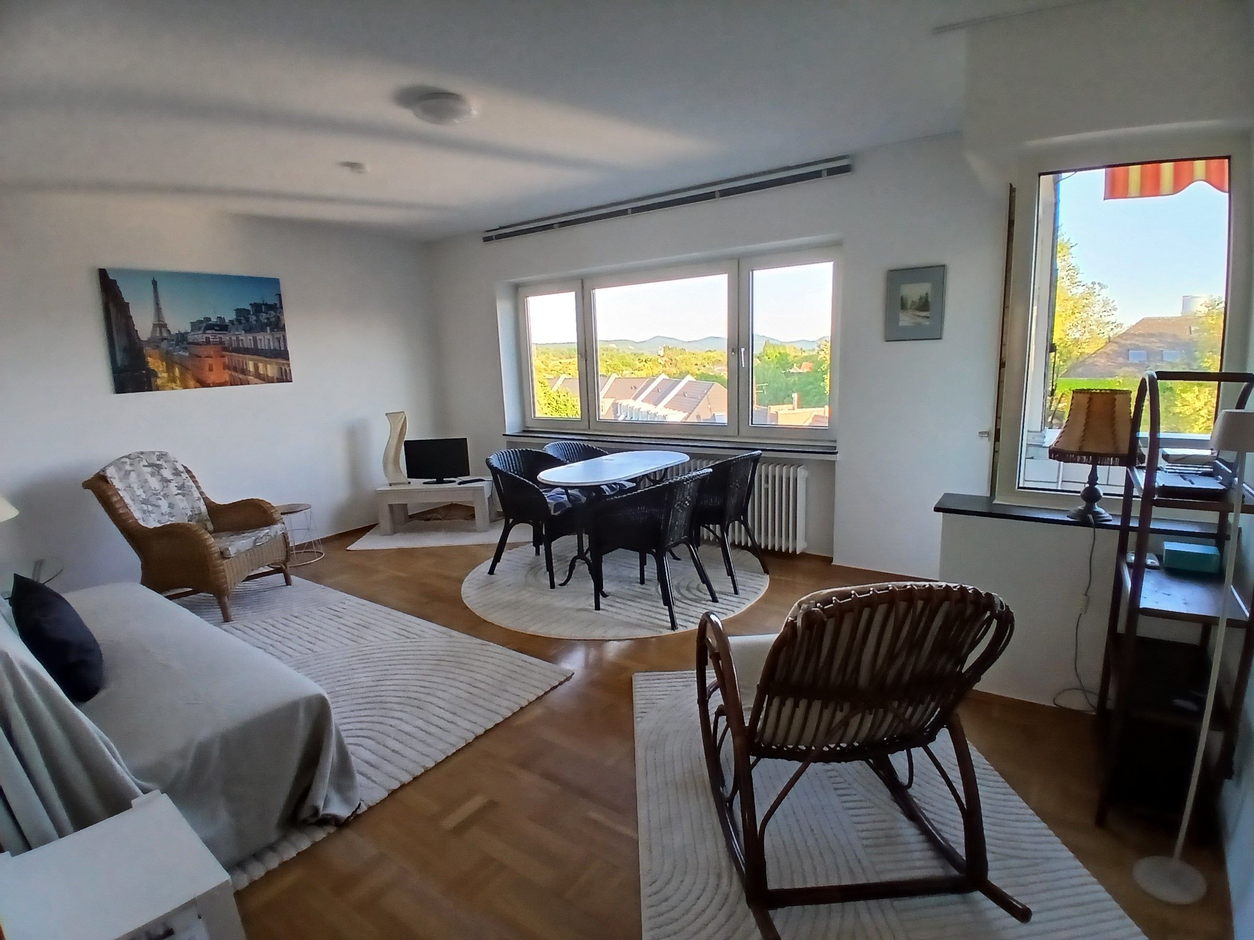 Una habitación con sofá, una mesa de comedor con sillas, un televisor sobre un mueble bajo y una ventana con vistas al campo.