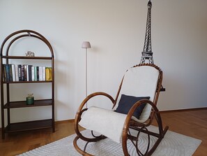 Una habitació amb una cadira d'oscill·la de vimet, una biblioteca amb llibres, una làmpada i una maqueta de la Torre Eiffel.