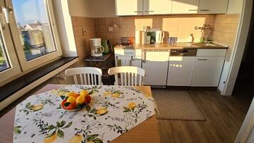 Una cocina con armarios blancos, una mesa de comedor con un centro de frutas y vistas por una ventana.