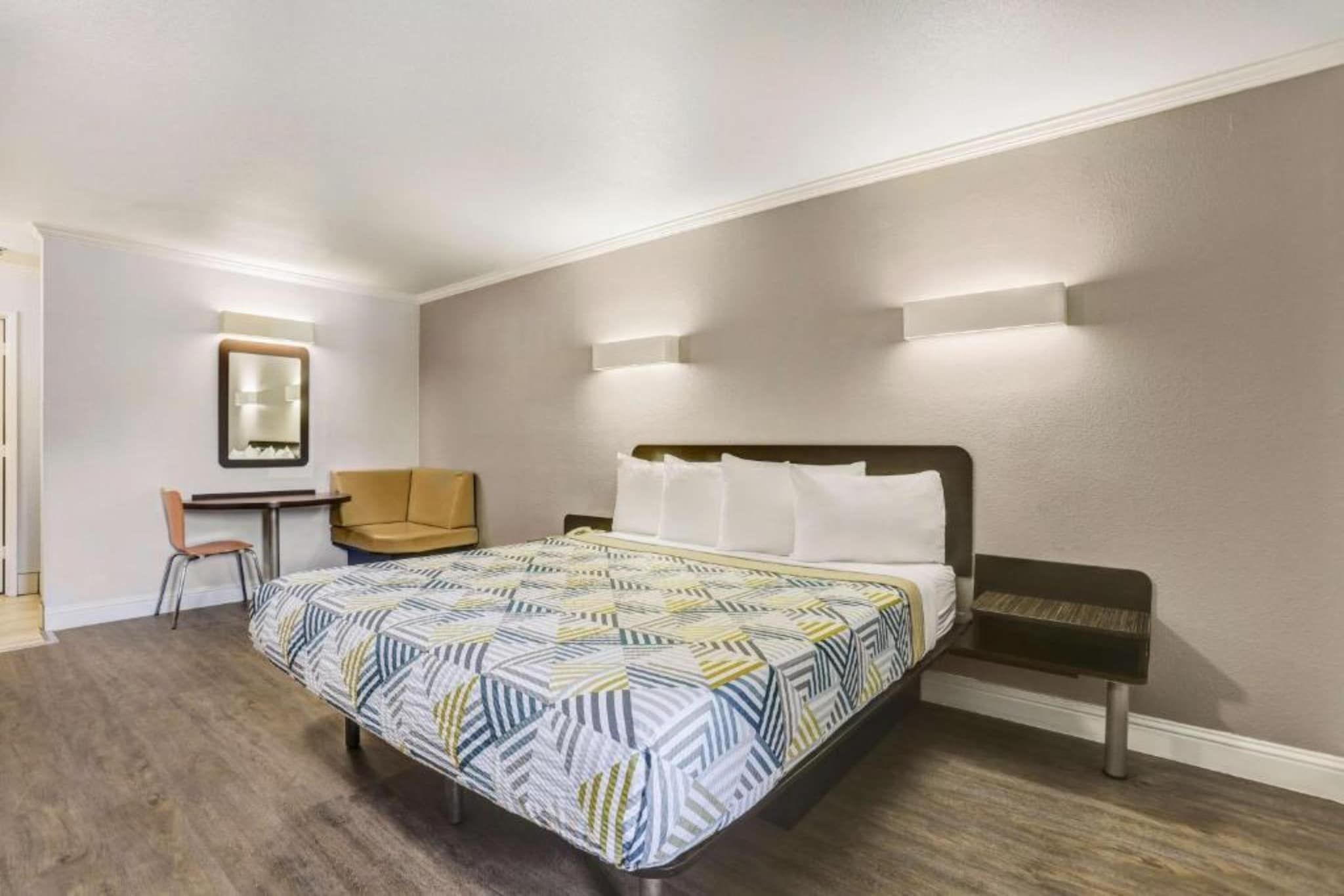 A hotel room with a bed, a desk, a chair, and a mirror.