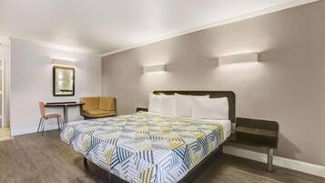 A hotel room with a bed, a desk, a chair, and a mirror.