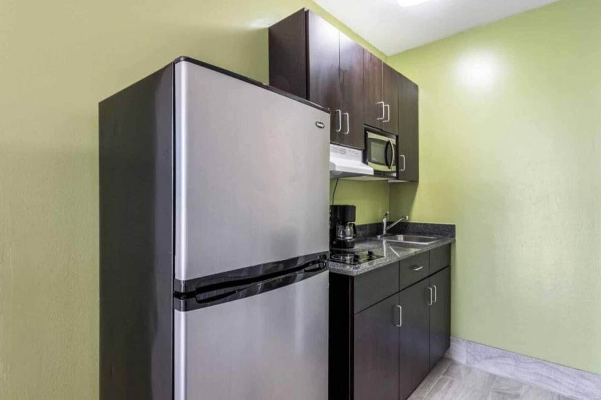 A compact kitchen with a stainless steel refrigerator, a microwave, and dark wooden cabinets.