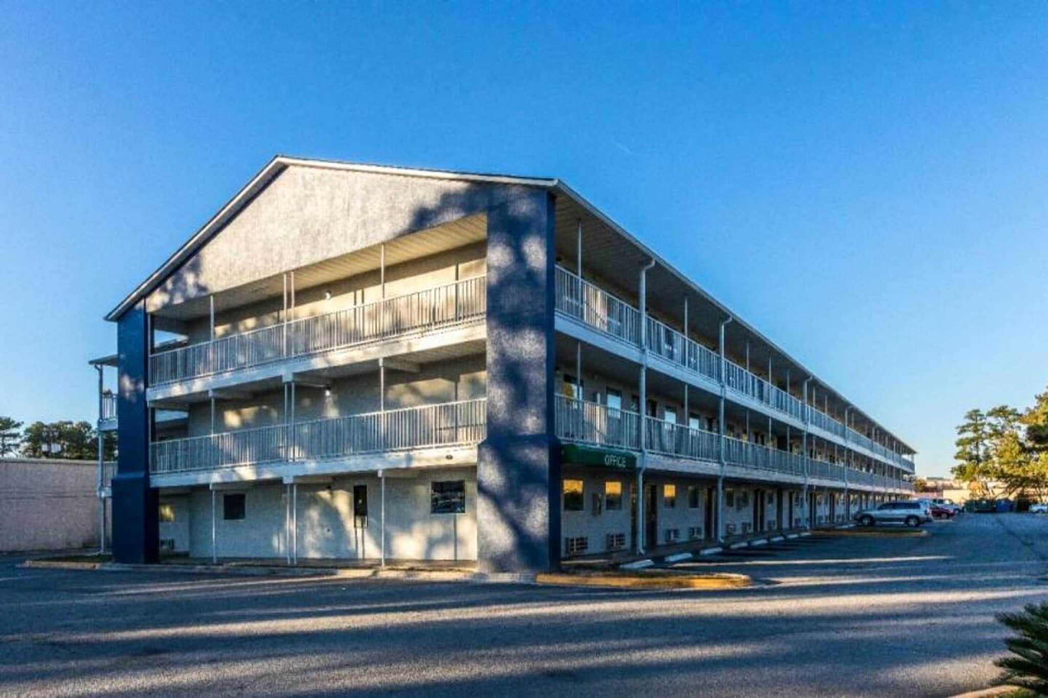 A multi-story building with balconies, a parking lot, and a clear sky.