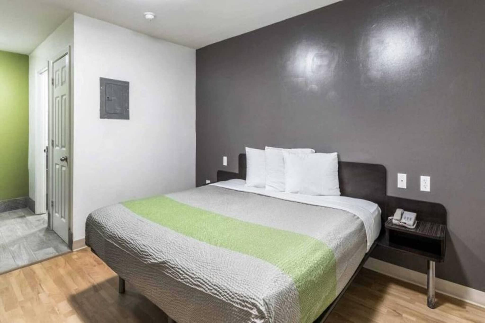 A hotel room with a bed, a nightstand, a telephone, and a door.