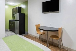 A room with a bed, a small kitchenette, a TV mounted on the wall, and two chairs around a table. - 1 queen bed | kitchen non-smoking (Savannah GA)