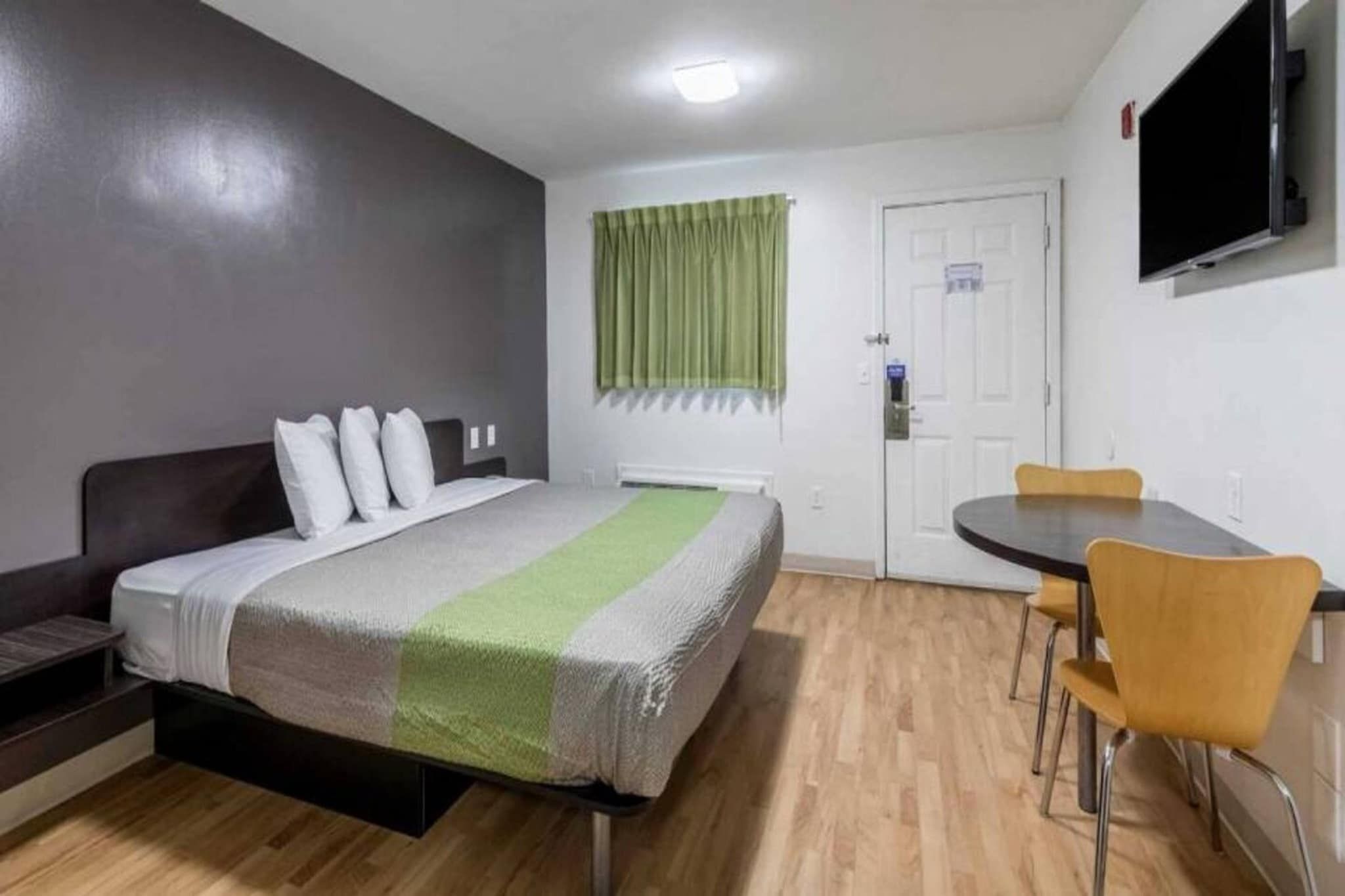 A bedroom with a bed, a desk, a chair, a television, and a door.