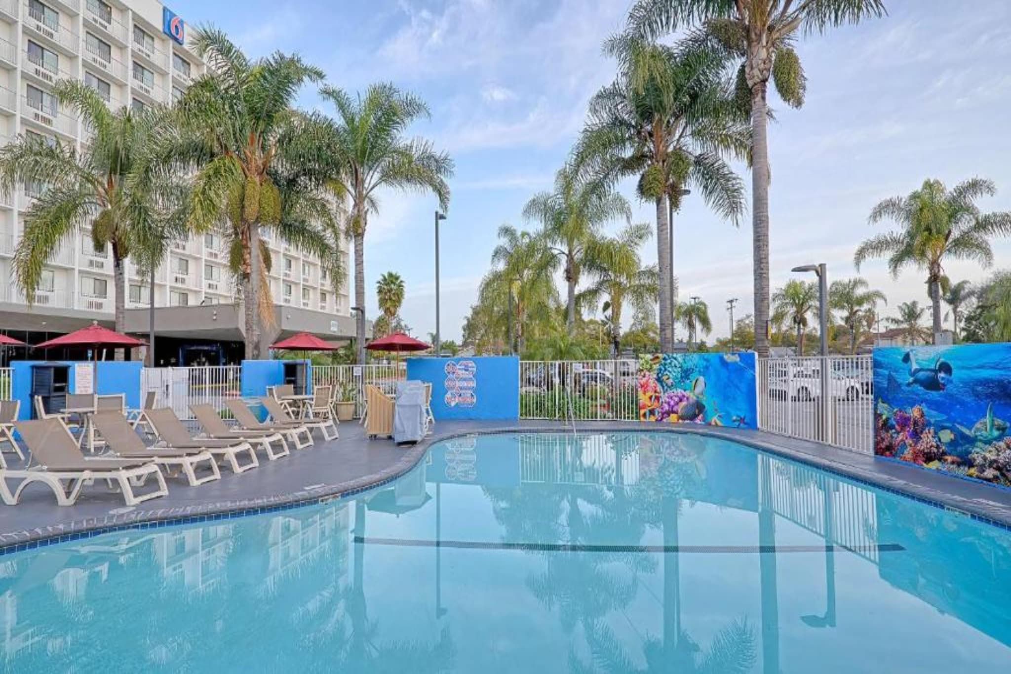 A swimming pool with lounge chairs and palm trees, surrounded by a hotel building.