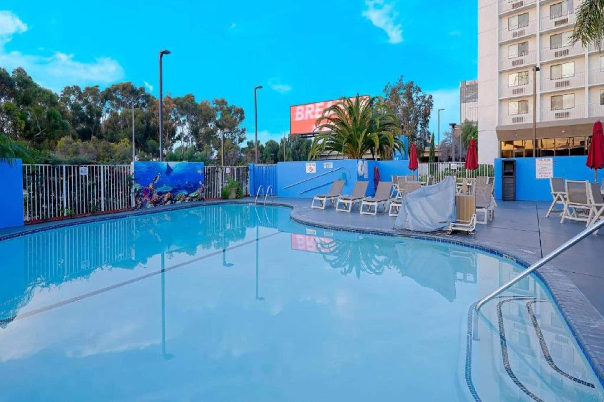 A clear swimming pool with lounge chairs and umbrellas, surrounded by a fence and trees.