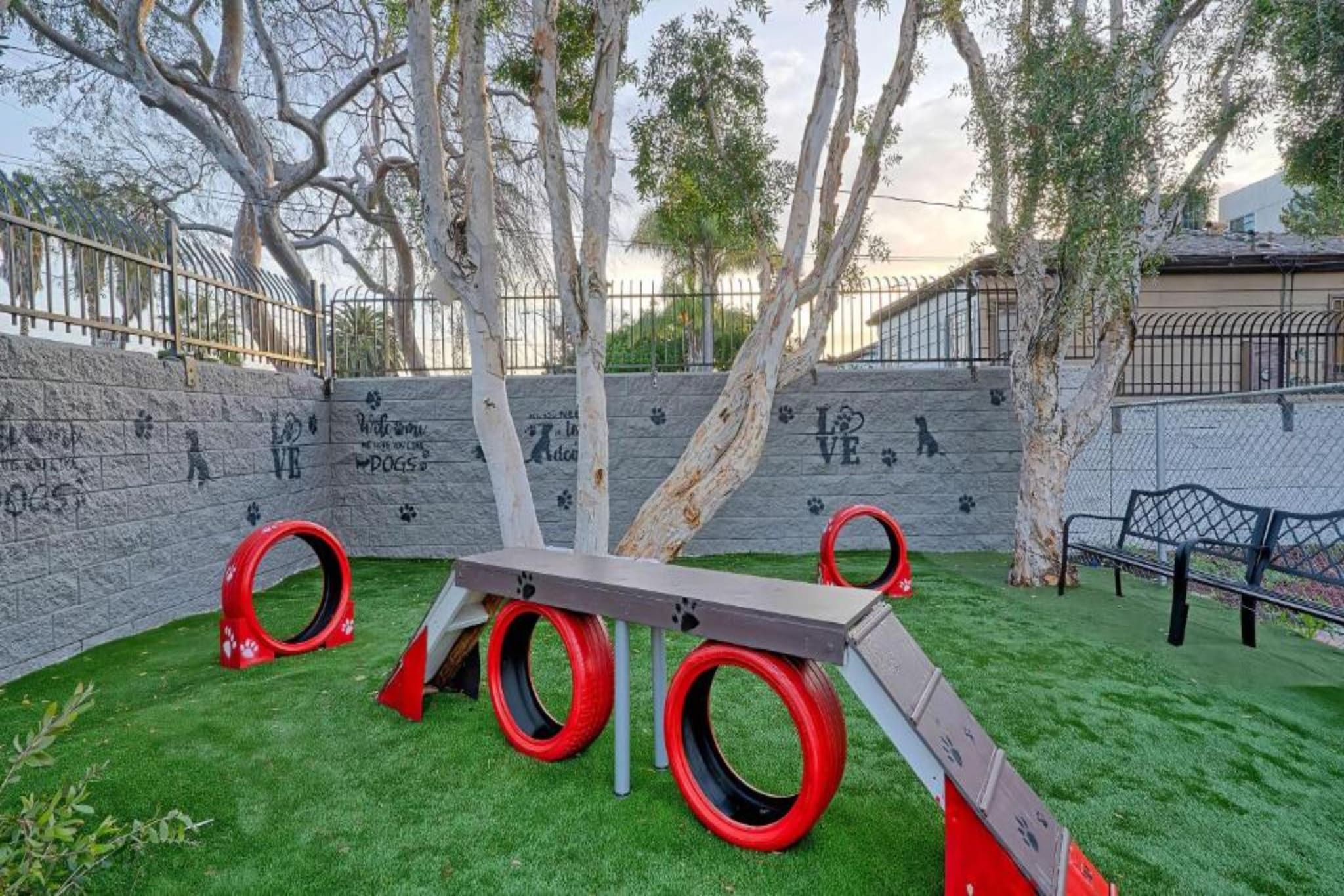 A playground with a seesaw and tire swings, surrounded by a stone wall with graffiti.