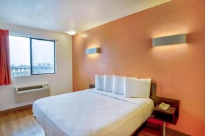 Une chambre d’hôtel avec un grand lit, une fenêtre, un appareil de climatisation, une table de chevet avec un téléphone et un luminaire fixé au mur.