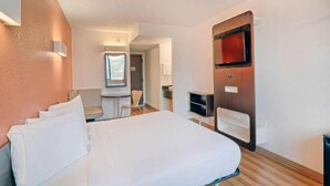Et hotelværelse med seng, skrivebord, stol, fjernsyn og et vindue.