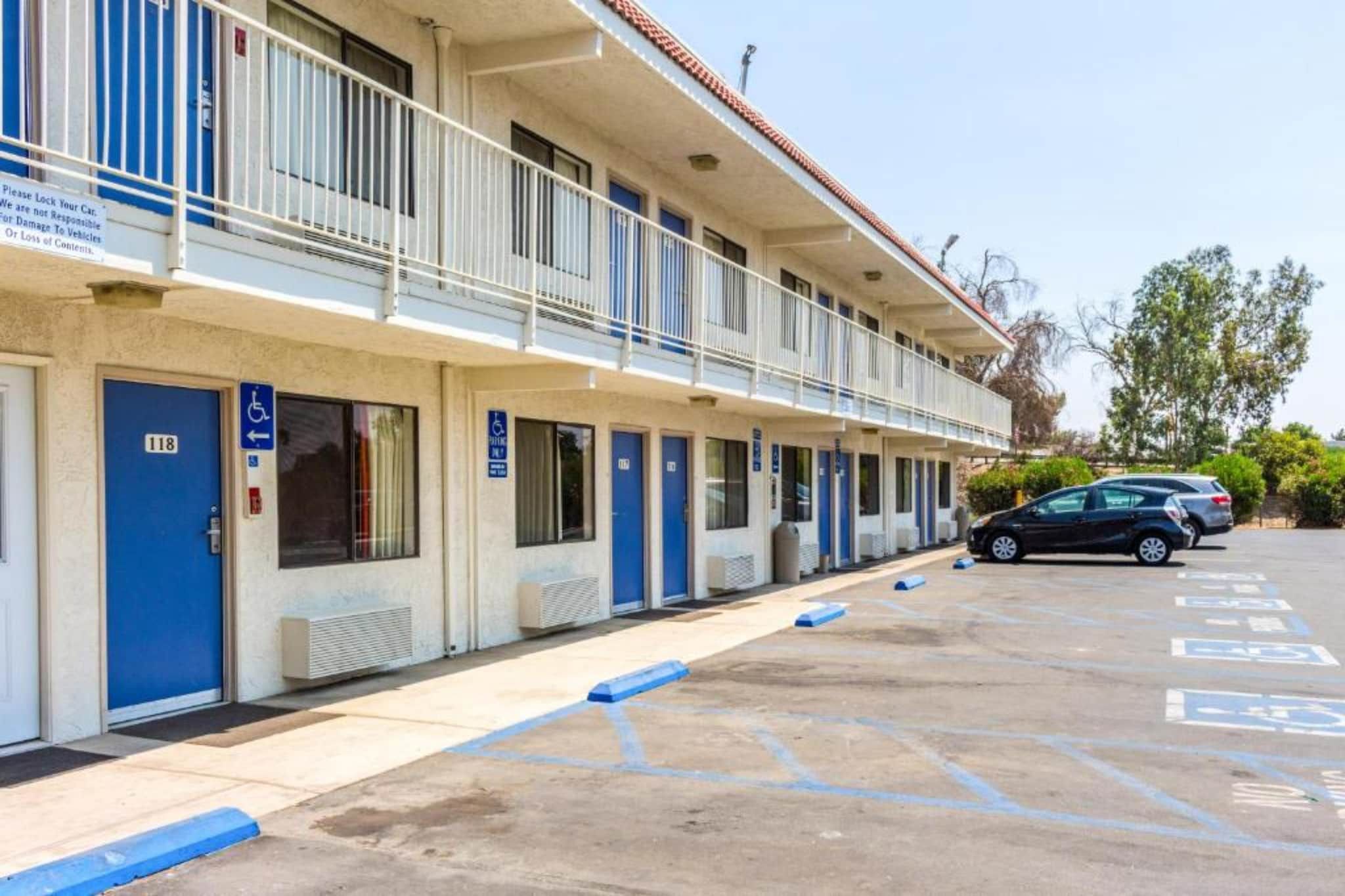 Ein Motel mit einer Reihe von Zimmern, jedes mit einer blauen Tür und einem barrierefreien Eingang. Es gibt einen Parkplatz mit ausgewiesenen Behindertenparkplätzen.