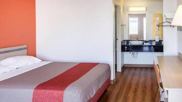 Habitación de hotel con una cama, un escritorio y un baño visible a través de una puerta abierta.