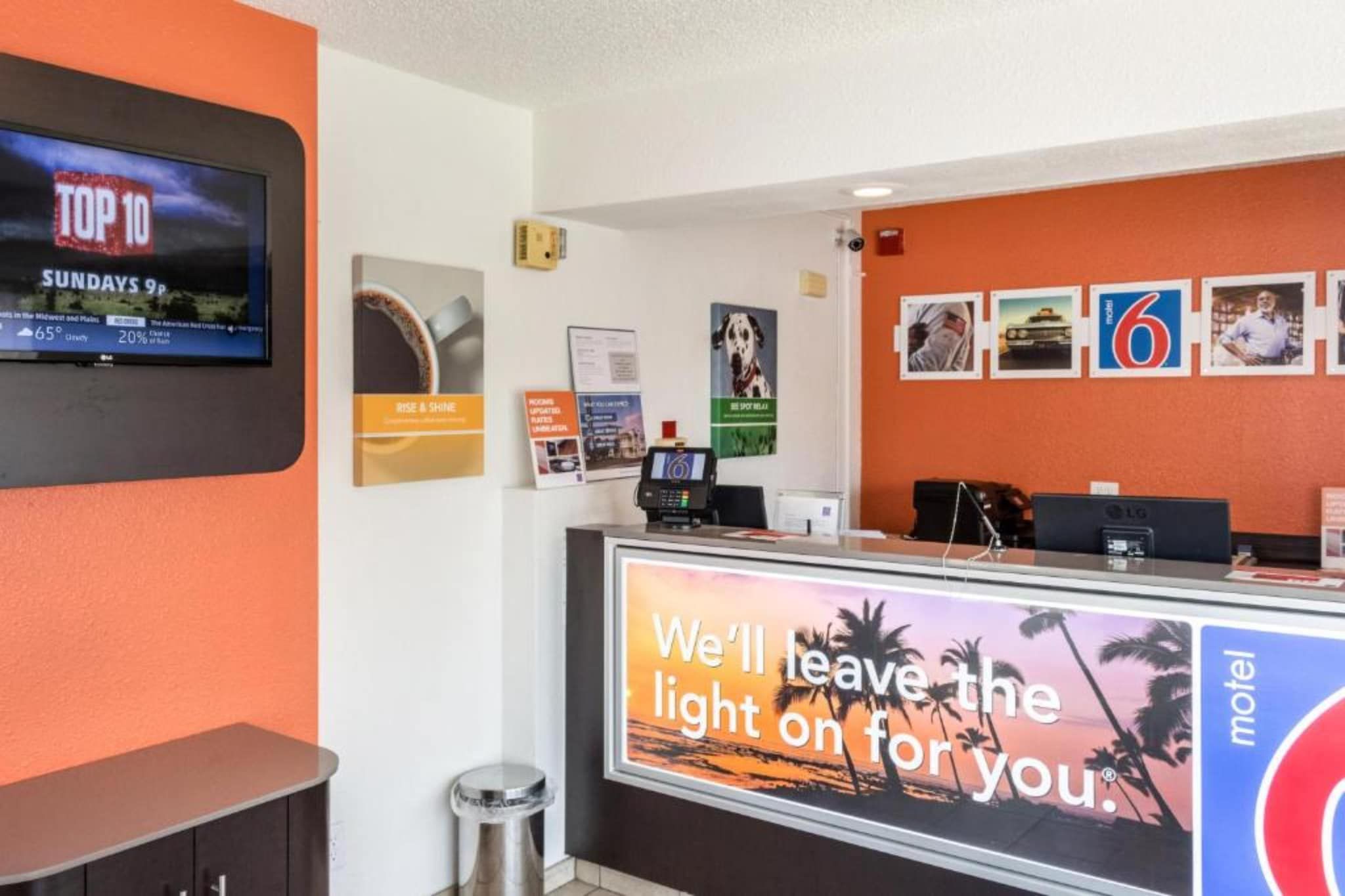 A hotel reception area with a TV displaying weather information, a digital kiosk, and a large sign with a motivational message.