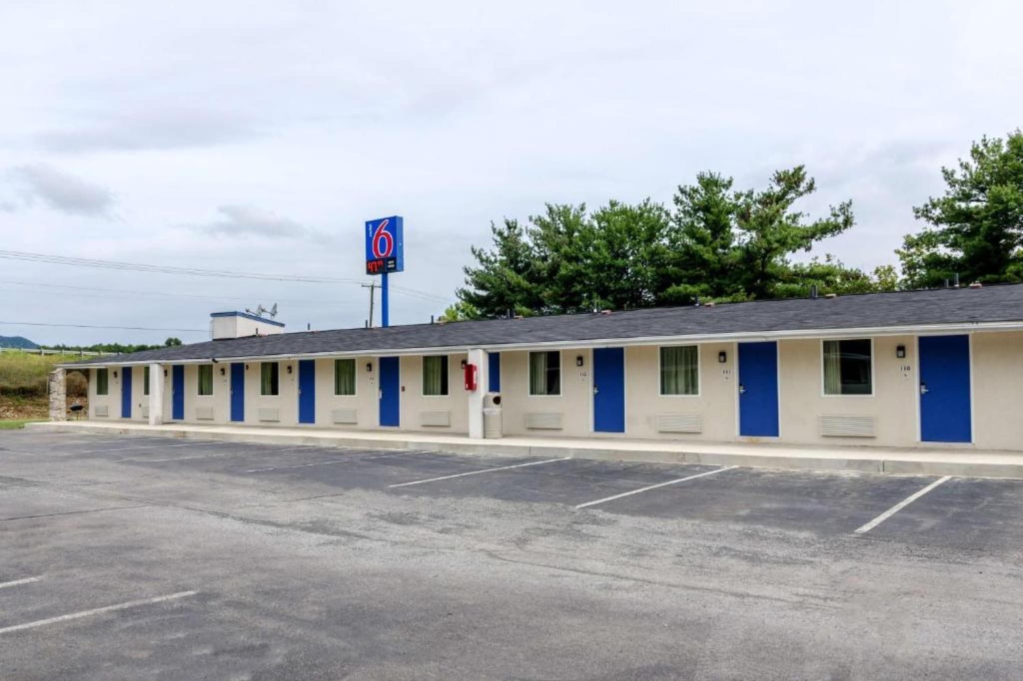 Un motel con una hilera de habitaciones, cada una con una puerta y una ventana. Hay un estacionamiento al frente.