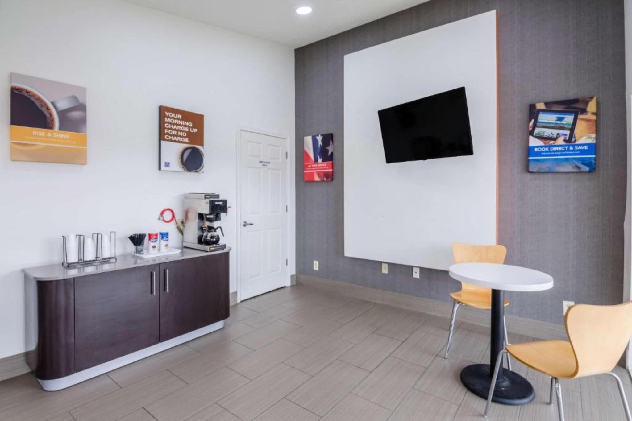 A modern office space with a reception desk, coffee machine, and a flat-screen TV mounted on the wall.