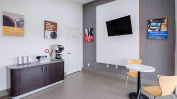 Un espacio de oficina moderno con mostrador de recepción, máquina de café y televisor de pantalla plana montado en la pared.