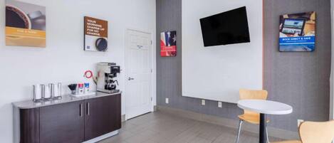 Un espace de bureau moderne doté d’un comptoir d’accueil, d’une machine à café et d’un téléviseur à écran plat fixé au mur.