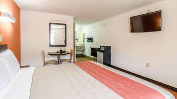 A hotel room with a bed, a desk, a chair, a television, and a kitchenette.