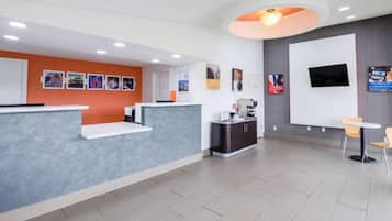 A reception area with a counter, seating, a coffee machine, and a TV on the wall.