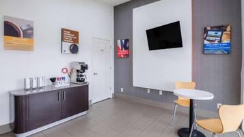 Un espace de bureau moderne doté d’un comptoir d’accueil, d’une machine à café et d’un téléviseur à écran plat fixé au mur.