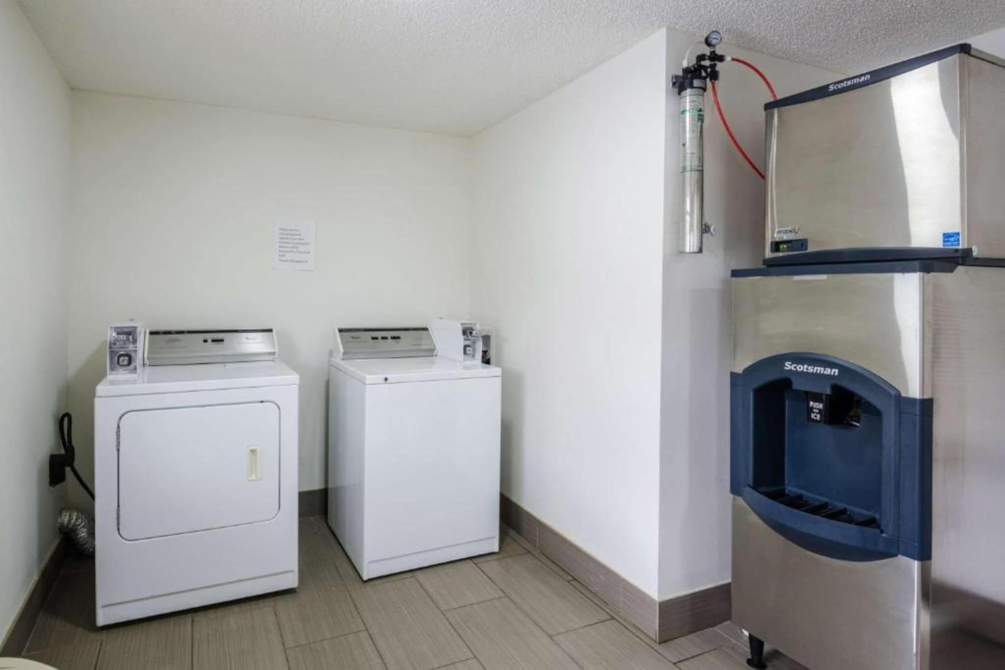 A laundry area with two front-loading washing machines and a stainless steel refrigerator with a water dispenser.