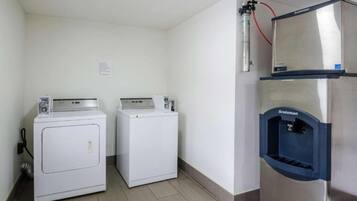 A laundry area with two front-loading washing machines and a stainless steel refrigerator with a water dispenser.