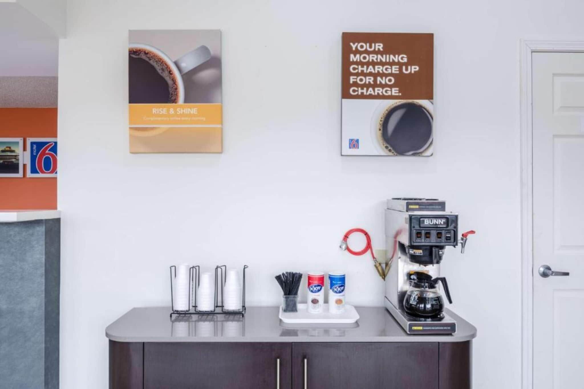 A coffee station with a coffee machine, cups, and a sign promoting a no-charge morning charge.