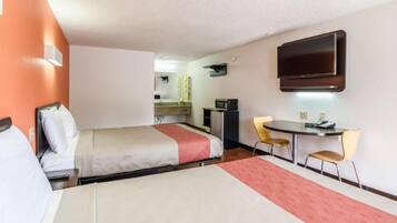 Habitación de hotel con cama, escritorio, silla, televisión y kitchenette.